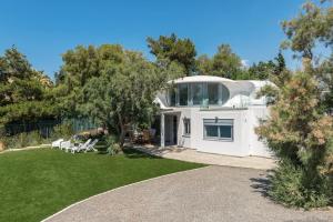 a white house with a yard with grass and trees at Villa Tholos -Athens Riviera in Kalívia Thorikoú