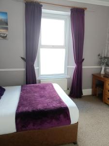 a bedroom with a bed with purple curtains and a window at Lawnswood Guest House in Torquay