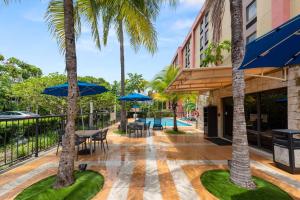 un patio con mesas, sillas y palmeras en Hampton Inn Miami-Airport West en Miami