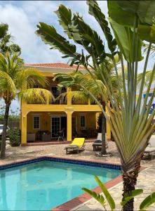 a pool in front of a yellow house with palm trees at Casa Makoshi Bonaire in Kralendijk