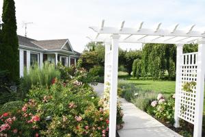 a white pergola in a garden with flowers at As You Like It Bed and Breakfast in Niagara-on-the-Lake