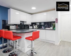 kuchnia z białymi szafkami i czerwonymi stołkami barowymi w obiekcie Spacious 5 Bedroom, 3 Bath House by Jesswood Properties Short Lets For Contractors, With Free Parking Near M1 & Luton Airport w Luton