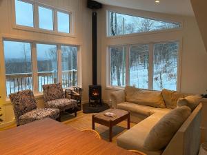 a living room with a couch and chairs and windows at Chalet avec Spa Baskatong in Mont-Laurier