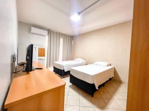 a room with two beds and a desk with a television at Apart Hotel em Brasília - Garvey Park Hotel in Brasília