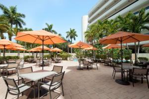 eine Außenterrasse mit Tischen, Stühlen und orangefarbenen Sonnenschirmen in der Unterkunft Embassy Suites Boca Raton in Boca Raton