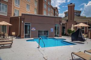 シャーロットにあるHilton Garden Inn Charlotte Pinevilleの中庭のスイミングプール(椅子、パラソル付)