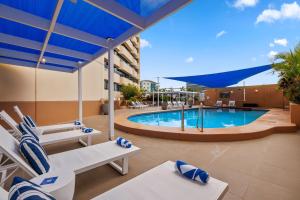 una piscina en un hotel con sillas y una sombrilla azul en Hilton Darwin en Darwin