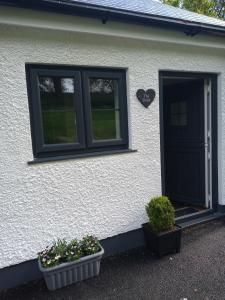 a white house with a black door and two plants at Vineyard Barns Gower in Swansea