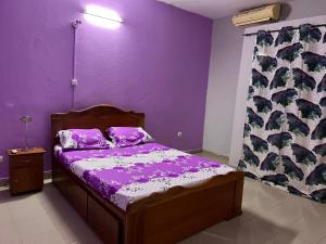 1 dormitorio con paredes de color púrpura y 1 cama con sábanas de color púrpura. en Ouedraogo Property Management, en Ouagadougou