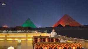 a man standing in front of the pyramids at night at Pyramids Height Hotel & Pyramids Master Scene Rooftop in Cairo