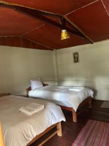 2 camas en una habitación con sábanas blancas en Refugio de Mery Lucmabamba, en Sahuayacu