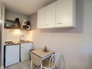 uma pequena cozinha com armários brancos e uma mesa e cadeiras em Studio Lamalou-les-Bains, 1 pièce, 2 personnes - FR-1-451-197 em Lamalou-les-Bains