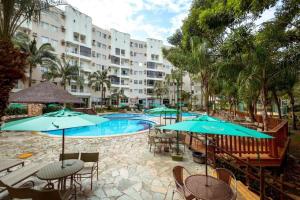 a swimming pool with tables and chairs and umbrellas at Thermas Paradise - Rio Quente - Apto 2 quartos com Suíte in Rio Quente