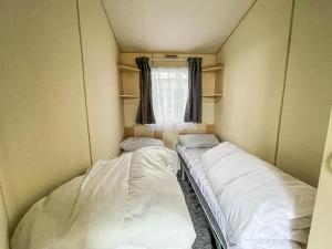 Duas camas num pequeno quarto com uma janela em Lovely Caravan At Valley Farm Holiday Park, Sleeps 8 Ref 46127v em Great Clacton