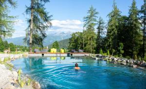 a person swimming in a pool with mountains in the background at Hotel Lärchenhof in Ramsau am Dachstein