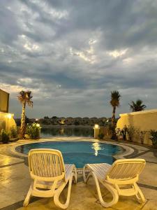 2 sillas sentadas junto a una piscina en شاليه فخم مع مسبح وبحر خاص بالخبر en Half Moon Bay