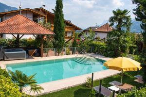 a swimming pool with an umbrella and a house at Hotel FleurAlp in Cermes
