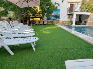 a row of white lounge chairs on the grass next to a swimming pool at Casa el angel in Castril