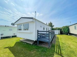 a white tiny house with a blue bench in a yard at Lovely 6 Berth Caravan With Decking, Close To The Beach In Suffolk Ref 68075bs in Lowestoft