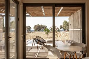 une porte en verre menant à une terrasse avec une table et des chaises. dans l'établissement Yenesis Seaside Retreat - Adults only, à Tinos