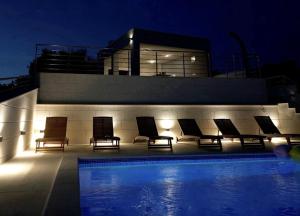 a group of chairs sitting next to a swimming pool at night at Villa Kiko - Primošten - Exclusively Yours - Private Pool & Panoramic Sea Views in Primošten +28 photos