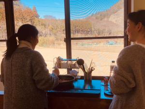 dos mujeres de pie en una cocina preparando comida en un tazón en Guest House「さごんヴィレッジ」, en Tsushima