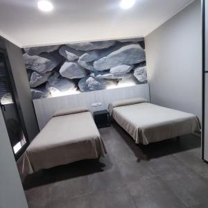 two beds in a room with a rock painting on the wall at Aparthotel Meseguer in Alcañiz