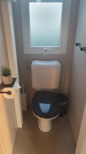 a bathroom with a toilet with a black seat and a window at Campingland Ostsee - Mobilheim 74Strandzauber NEU! in Schashagen