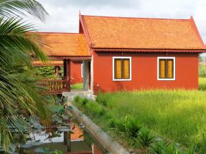 a red house with a pond in front of it at Toek Chha Temple Resort in Kampong Cham