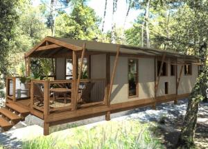 a cabin with a deck in the woods at Camping de la Dune "Les Flots Bleus" in Pyla-sur-Mer