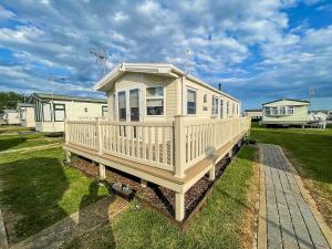 a large white house with a porch on the grass at Caravan With Decking And Free Wifi At Seawick Holiday Park Ref 27214sw in Clacton-on-Sea