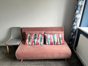 un sofá rosa con 2 almohadas y una silla en Godrevy Lighthouse View, Carbis Bay, St Ives, free parking near beach en Carbis Bay