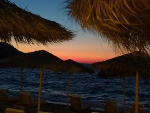 Una puesta de sol en la playa con sillas y sombrillas de paja. en Kokkari Social Club, en Kokkari
