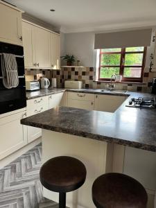 a kitchen with white cabinets and a counter with two stools at Wharf Cottage in Coalbrookdale