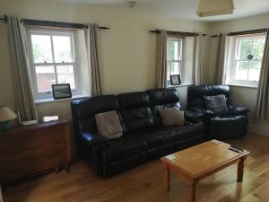a living room with a black leather couch and a table at Lovely 3-Bed House at Clashganny Mill Borris in Carlow