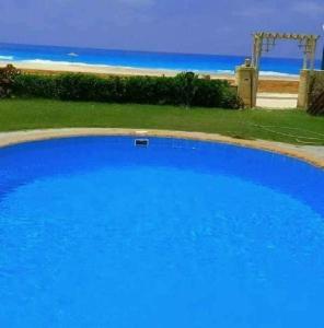 ein großer blauer Pool neben einem Strand in der Unterkunft الساحل الشمالي in Dawwār Abū Maḩrūs