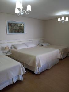 a room with three beds with white sheets at Pousada Serrano in Campos do Jordão