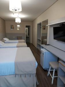 a hotel room with three beds and a flat screen tv at Pousada Serrano in Campos do Jordão