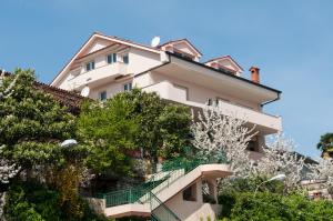 a tall white building with stairs in front of trees at Apartments Komel in Opatija