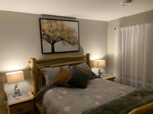 a bedroom with a bed with two lamps and a tree on the wall at Dragonfly Inn Walkout Suites in Sherwood Park
