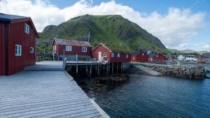 a group of red houses next to the water with a mountain at Real fisherman's cabins in Ballstad, Lofoten in Ballstad