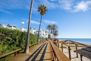 Beach Apartment La Cala de Mijas في لا كالا ذي ميخاس: ممشى خشبي يؤدي إلى الشاطئ وبه أشجار نخيل