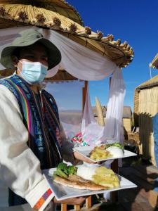 una mujer con una máscara sosteniendo dos platos de comida en Uros Tikarani hotel, en Puno