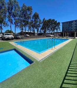 una gran piscina con agua azul y césped verde en Departamento full equipamiento, en San Pedro de la Paz