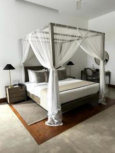 um quarto com uma cama de dossel e cortinas brancas em The Villa by Contemporary Ceylon em Wadduwa