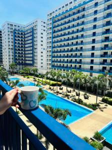 een persoon met een koffiekopje op een balkon met uitzicht op een zwembad bij Sea Residences - Call Ang Alano in Manilla