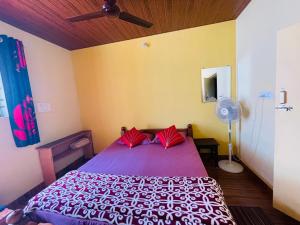 NEW ORGANIC HOME STAY في Mudigere: غرفة نوم مع سرير أرجواني مع وسائد حمراء ومروحة
