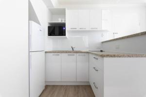 a white kitchen with white cabinets and a refrigerator at Resort Living, Luxury Getaway, Close 2 Noosa River in Noosaville