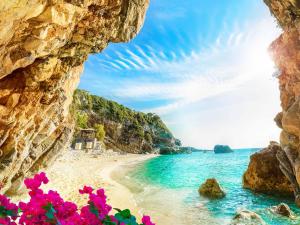 a view of a beach from a cave with pink flowers at Pentofanoro Central Studio - Corfu Cozy Getaway in Corfu