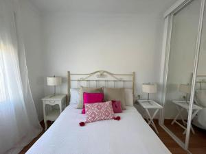 Una gran cama blanca con almohadas rosas. en Precioso apartamento con piscina, en Castelldefels